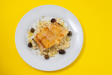 fried cod fish with cous cous and olives on white plate