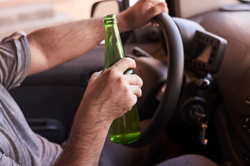An unrecognizable man drinking beer while driving car. Concepts of driving under the influence, drunk driving or impaired driving