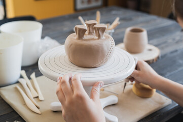 Closeup of bottom of mug, which is being decorated in ceramic studio. Female professional hands making clay dots or drops on the surface of vase by special squeezing tool.