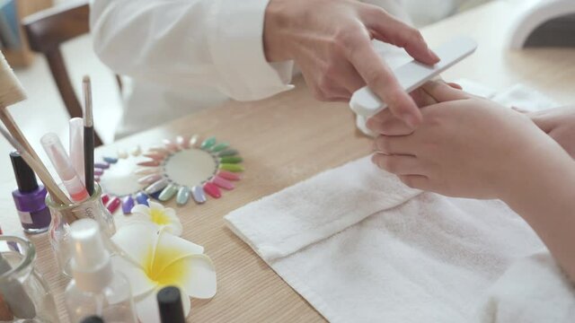 Close up view of female hands of qualified manicurist filing nails of young woman customer with white buffer in trendy nail salon. manicure process concept. beautician lady holding client hand