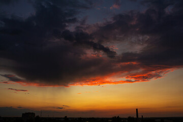Naklejka premium Black thunderclouds at sunset. Bright orange sunset and dark clouds. Storm sky