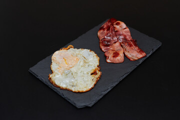 an egg and two pieces of bacon on top of a black board