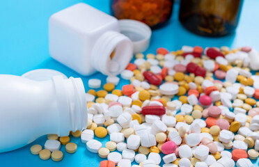 Medical pills and tablets spilling out of a drug bottle on blue background