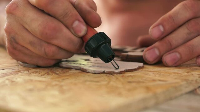 Concept on the theme of craft wood. Close up of artist's hand drawing on a wooden board by burning. Decorative articles made of wood