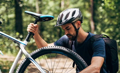 Outdoor image of professional cyclist man fixing a bicycle brake during riding the bike on the mountain.