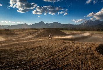Motocross ride on dry dirt track full of dust. Late afternoon summer day. Alps mountains in the distance