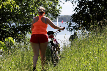 Overweight woman in shorts riding bicycle to the beach, selective focus. Girl cyclist, summer leisure on a coast, cycling and slimming concept