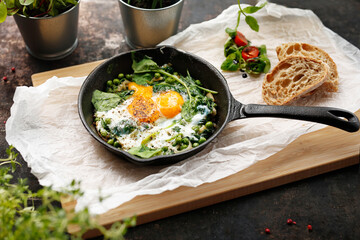 Eggs with green peas and spinach baked in a pan. Ready dish served in a hot pan. Suggestion of...
