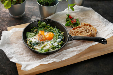 Shakshouka, eggs baked with green peas and spinach. Ready dish served in a hot pan. Suggestion of serving the dish. food background