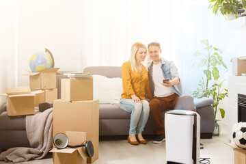 Fototapeta na wymiar Young caucasian man and woman sitting on sofa. Near stay white modern air purifier. Air purity and healthcare concept.