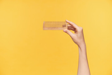 Cropped shot of young female's hand being raised while holding wooden hairbrush with forefinger and...