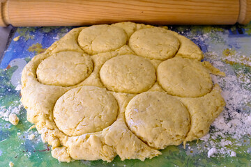 Home baking: Savoury scone dough cut into rings ready for baking with a wooden rolling pin in the background. 