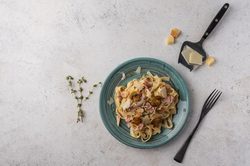 Top view pasta fettuccine with mushrooms, bacon and parmesan cheese in white plate with fork on a light wooden background with copy space