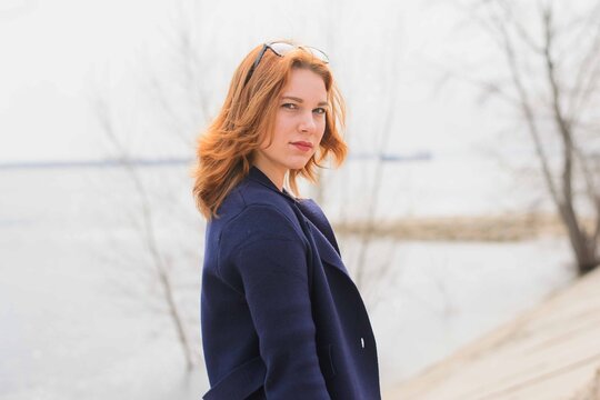 portrait of a red-haired, young girl in blue polto walking along the promenade