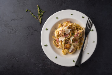 Top view pasta fettuccine with mushrooms, bacon and parmesan cheese in white plate on a dark graphite wooden background with copy space