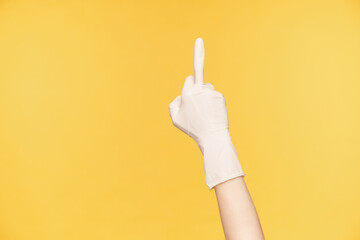 Studio photo of raised hand being raised while expressing negative emotions, showing middle finger while being isolated over orange background. Human hands and emotions