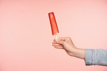 Studio photo of delicious ice-cream on stick being held by young female's hand with nude manicure...