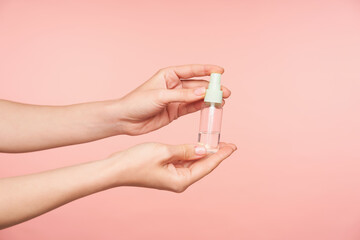 Indoor shot of raised female's hand with nude manicure holding spray bottle with disinfectant while...