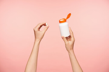 Indoor shot of bottle with vitamins being held by young fair-skinned female's hands being isolated...