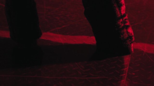 Black shaggy legs with hooves. Devil's feet in red light walk on the floor