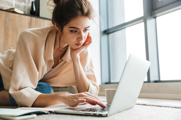 Fototapeta premium Image of focused woman working with laptop while sitting on floor