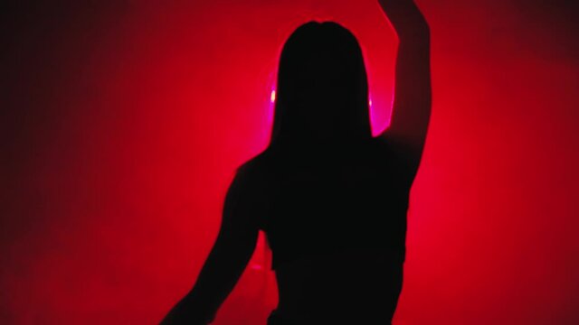 Silhouette of a dancing girl with long hair on a red background in slow motion