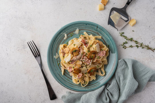 Top view pasta fettuccine with mushrooms, bacon, parmesan cheese in white plate with fork and napkin on a light wooden background with copy space
