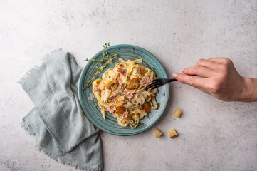 Woman's hand holds a fork with pasta fettuccine with mushrooms, bacon, parmesan and bechamel sauce...