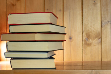 Book stack lit from behind on a wooden bookcase with copy space to the right hand side and lit from behind