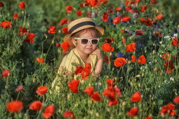 Portrait of a little girl in a field with poppies .A child in a straw hat and sunglasses