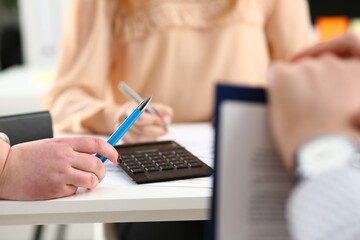 Close up of young man holding blue pen while sitting at the table with calculator and working with...