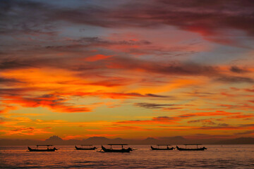 Fishermen boats silhouettes in tropical fiery sunset light. View from Kuta beach, Bali island, Indonesia 