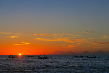 Fototapeta premium Vibrant colours beautiful ocean sunset with dark fishermen boats silhouettes at Kuta beach, Bali, Indonesia