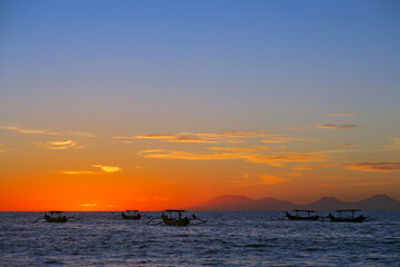Fototapeta na wymiar Vibrant colours beautiful ocean sunset with dark fishermen boats silhouettes at Kuta beach, Bali, Indonesia