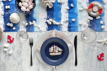 Columbus Day table setting with nautical sea decorations on blue and white stripy runner, classic blue white plates, utensils on white rustic table. Top view, casual modern lunch.