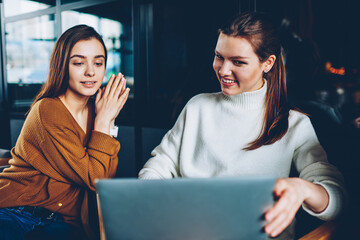 Cheerful hipster girls making video call using web camera on netbook device connected to wifi...