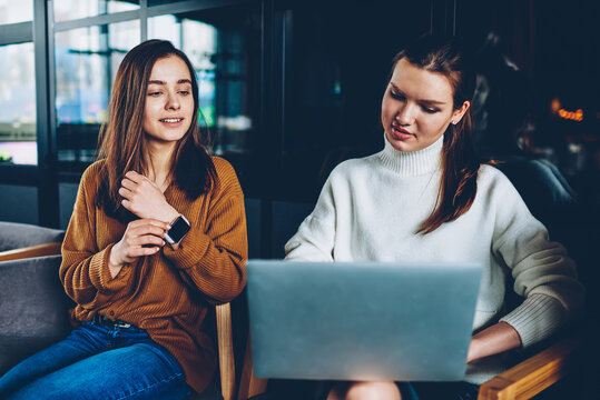 Positive female student watching funny video with friend using laptop device connected to cafeteria wifi, two successful women browsing wireless internet for download file resting at cafeteria