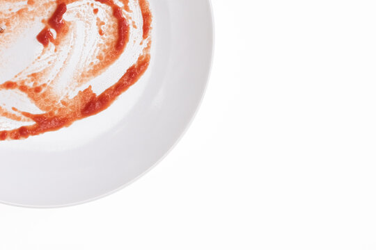 Empty dirty white plate after spaghetti with tomato sause or ketchup on it on white background with copy space