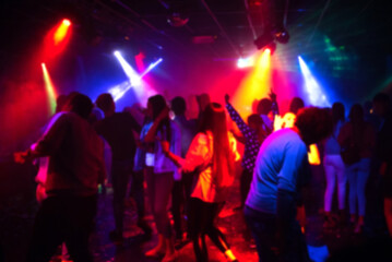 blurred silhouettes of a group of people dancing in a nightclub on the dance floor under colorful...