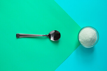 Collagen protein powder in jar and spoon on green background.