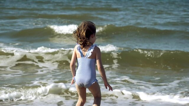 Little kid girl plays on Baltic sea beash shallow waterline summer rest during vacations