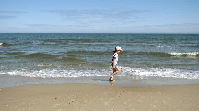 Little kid girl plays on Baltic sea beash shallow waterline summer rest during vacations
