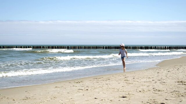 Little kid girl plays on Baltic sea beash shallow waterline summer rest during vacations