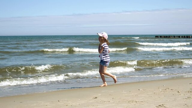 Little kid girl plays on Baltic sea beash shallow waterline summer rest during vacations