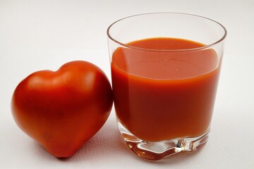 Glass of fresh tomato juice and red tomato on a white background