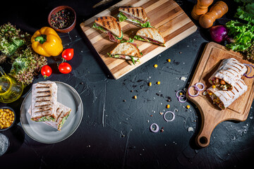 Shawarma sandwich with grilled meat, mushrooms, cheese, cabbage, carrots, sauce, green and sandwich with ham on dark background