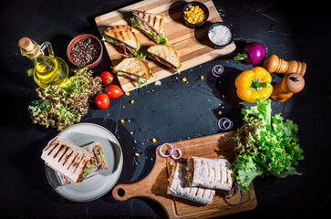 Shawarma sandwich with grilled meat, mushrooms, cheese, cabbage, carrots, sauce, green and sandwich with ham on dark background