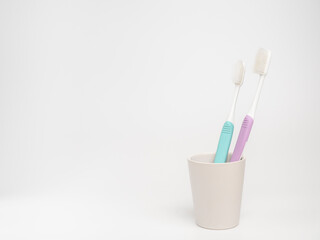 Old used pastel toothbrush in ceramic cup on white background.