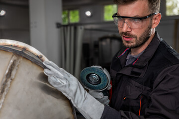 Industrial worker with angle grinder working and polishing metal structure at workshop.