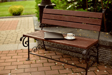 
laptop and cup of tea on a bench in a city park.